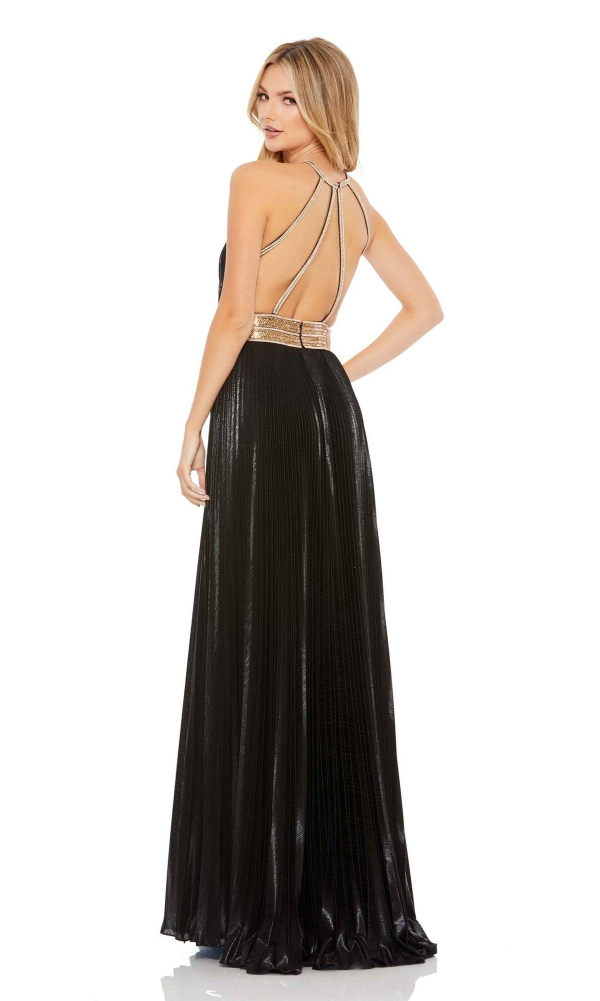 A woman wearing the Long Formal Dress 30722 by Mac Duggal—floor-length, pleated black metallic gown with a gold belt and open back—poses with one hand on her hip, looking over her shoulder.